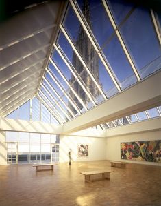 a person standing in an empty room with large windows and artwork on the wall behind them