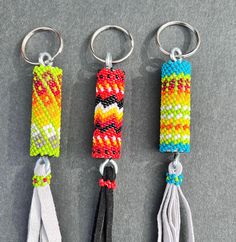 three key chains with different colored beads and tassels hanging from them on a gray surface