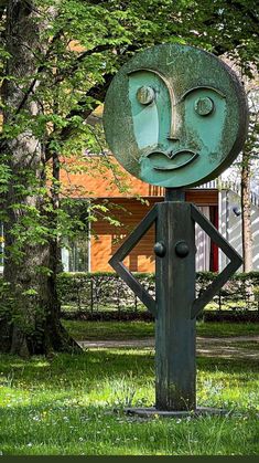 a metal sculpture with a face on it in the middle of some grass and trees