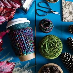 yarn, scissors and other crafting supplies on a blue surface with leaves in the background