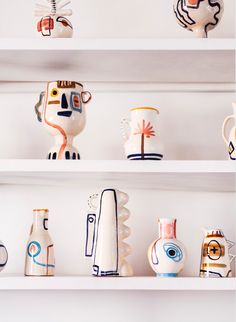 many different vases are on shelves with white walls and one is blue, the other has orange