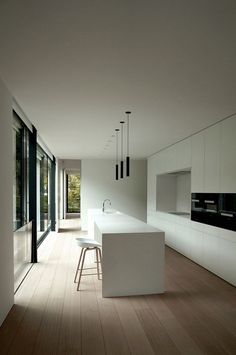 an empty kitchen with white counter tops and wooden flooring next to large glass windows