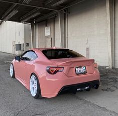 a pink sports car parked in front of a building with its hood up and tail lights on