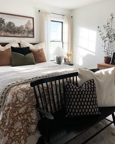 a bed sitting in a bedroom next to a window with white curtains and pillows on top of it