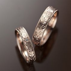 two wedding rings with engraved designs on each side and a diamond in the middle, set against a black background