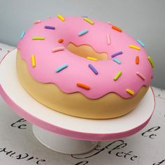 a pink frosted donut sitting on top of a white cake plate