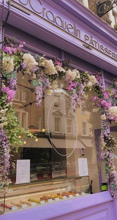 a purple store front with flowers hanging from it's glass display case and windows