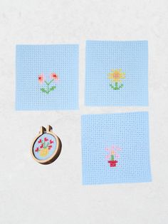 four cross - stitch coasters with flowers on them and a small wooden brooch