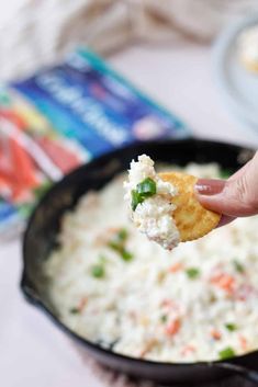 a hand holding up a piece of food in a skillet filled with rice and vegetables