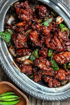 a metal bowl filled with meat and vegetables on top of a wooden table next to green beans