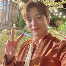 a young man making the peace sign in front of a tree with lights on it