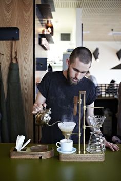 a man pours coffee from a glass pitcher into a cup on top of a wooden tray