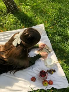 a woman laying in the grass reading a book and eating fruit on top of it