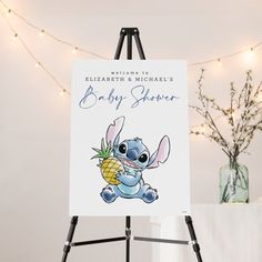 a baby shower sign on an easel next to a vase with flowers in it