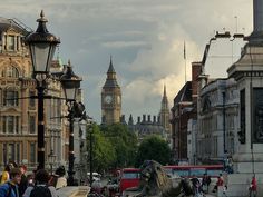 people are walking on the sidewalk in front of some buildings and a clock tower with a steeple