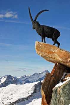 a goat statue sitting on top of a tree stump in the snow with mountains in the background