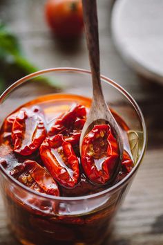 a spoon full of sliced red peppers on top of a glass cup filled with liquid