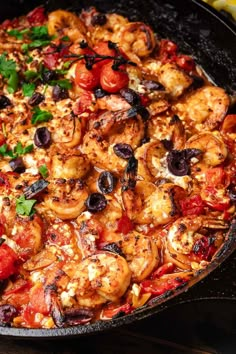 a skillet filled with shrimp, tomatoes and olives