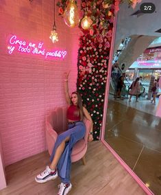 a woman sitting on a pink chair in front of a wall with flowers and lights