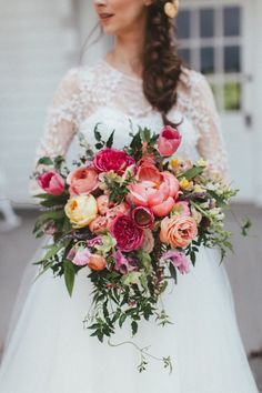 a woman holding a bouquet of flowers in her hand and wearing a wedding dress with lace sleeves