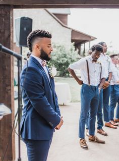 a group of men standing next to each other in front of a building and one man is wearing a blue suit