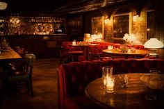 a dimly lit restaurant with red velvet chairs and wooden tables in front of the bar