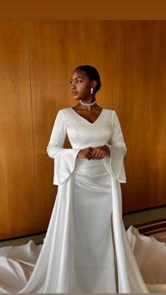 a woman in a white dress standing next to a wooden wall