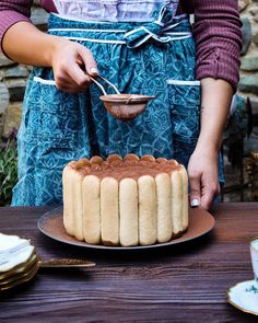 a woman in an apron holding a spoon over a cake