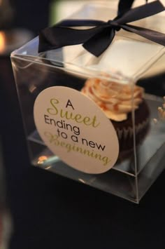 a cupcake in a clear box with a black bow on the top that says a sweet ending to a new beginning