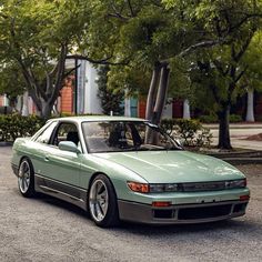 a green car parked in front of some trees