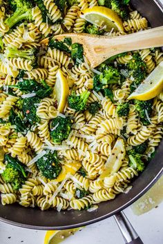 a skillet filled with pasta, broccoli and lemon wedges