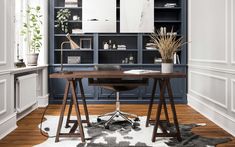 a home office with blue bookcases and wooden desk in the center, along with an area rug on the floor