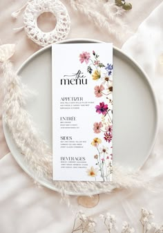 the menu card is sitting on top of a plate with white feathers and flowers around it