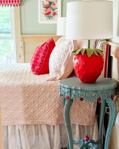 a blue table with a strawberry on it next to a white lamp and red pillows