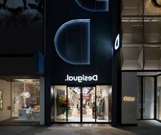 the entrance to an upscale clothing store lit up at night with large letters on it