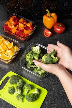 the person is cutting up broccoli on the counter with other vegetables in plastic containers