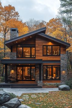 a modern house in the woods surrounded by rocks and autumn trees with leaves on the ground