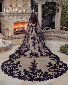 a woman standing in front of a fireplace wearing a black wedding dress with flowers on it