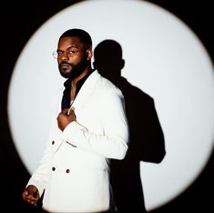 a man standing in front of a white wall wearing a suit and tie with his hands on his chest