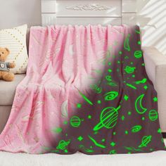 a teddy bear sitting on a couch next to a pink blanket with green planets and stars