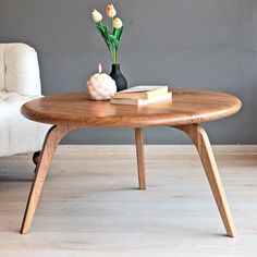 a coffee table with flowers and books on it in front of a white chair next to a gray wall