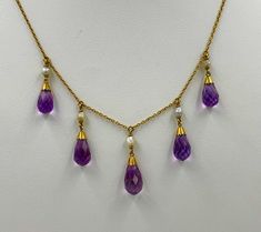 A stunning Victorian - Belle Epoque Amethyst Necklace with 5 gorgeous graduated Briolette Cut Amethysts set in a perfect 14 Karat Yellow Gold Necklace. The Amethysts have the most wonderful purple color and the briolette cut of the gems brings out their vivid beauty. The amethysts are graduated giving the necklace such balance and beauty. The amethysts hang from lovely natural white pearls set in 14 Karat Gold. The necklace is full of the romance and delicate style of the Victorian - Edwardian era. A perfect jewel for everyday or for the most glamorous affair. The gold is the most beautiful antique gold with the warmth and color we all just love. The necklace hangs beautifully around the neck. The design is full of the delicate romance of the age and is so special with the amethysts which Amethyst Set, Antique Jewelry Necklace, Yellow Gold Necklace, Necklace Antique, Wire Necklace, Edwardian Era, Pearl Set, Amethyst Necklace, Vintage Watches