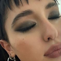 a close up of a woman with black hair and silver eyeshadow wearing large hoop earrings