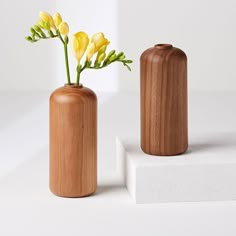 two wooden vases with flowers in them sitting on a white surface next to each other