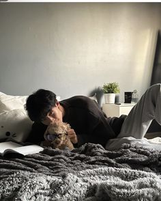 a man laying on top of a bed holding a teddy bear next to his face