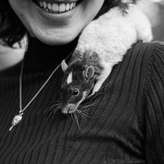 a woman is holding a small rodent on her shoulder and smiling at the camera