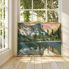 a painting is hanging on the wall in front of a window with a view of mountains and lake