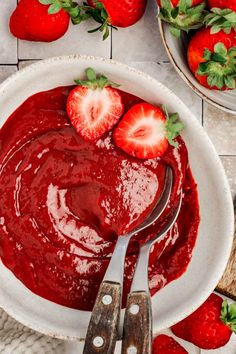 a bowl of strawberry jam with two strawberries on the side