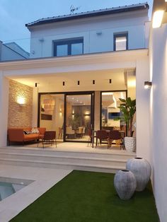 a modern house is lit up at night with lights on the patio and lawn area