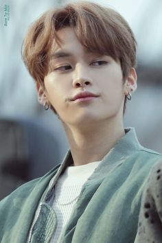 a young man with ear piercings on his ears and wearing a green jacket, looking at the camera